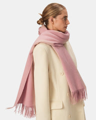 A woman in a white coat elegantly wears a pink scarf, adding a touch of color to her outfit.