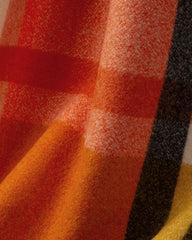 A close-up view of a cozy plaid scarf featuring vibrant red, orange, and black patterns.