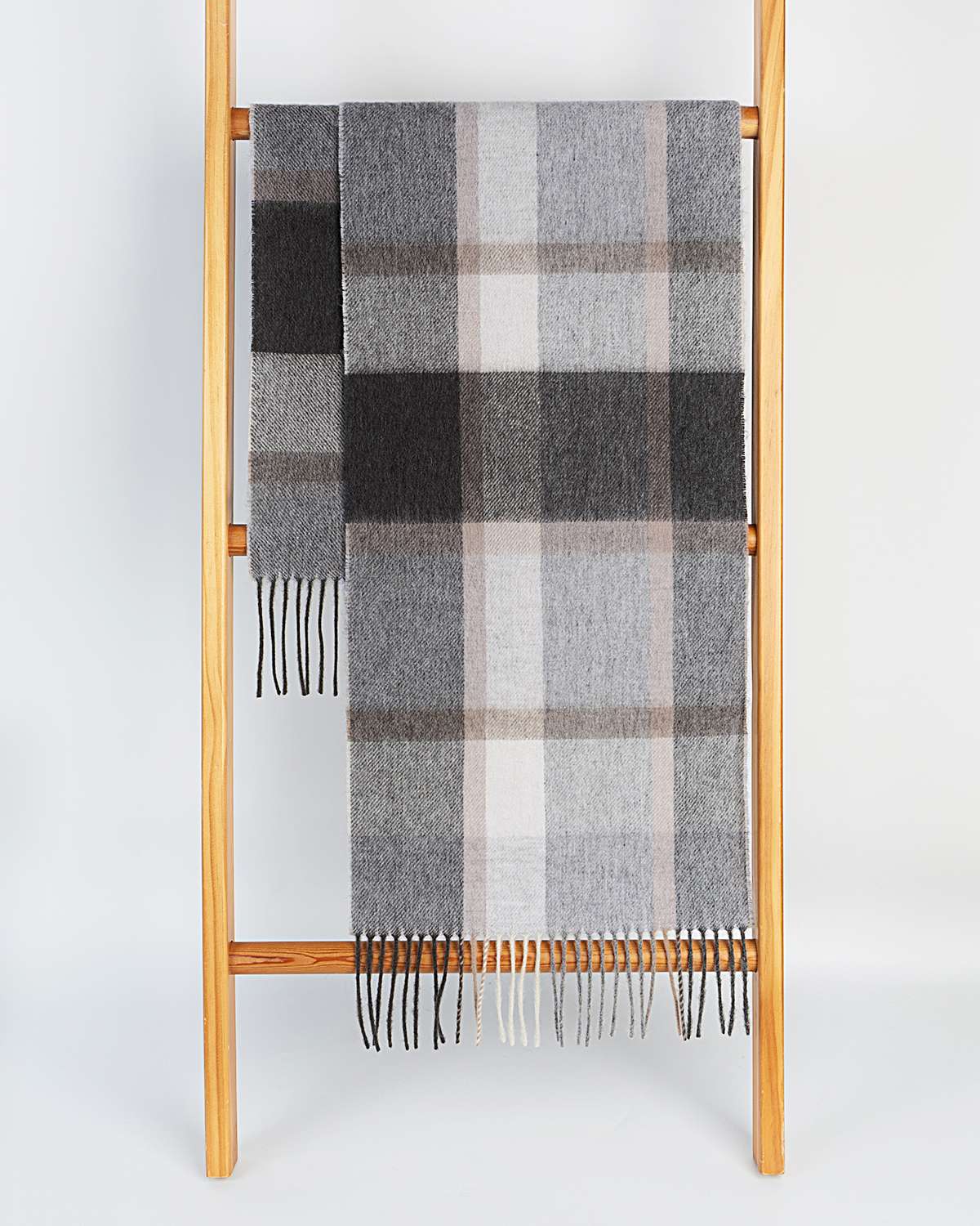 A gray and beige plaid winter scarf draped elegantly over a wooden ladder, showcasing its winter warmth and style.