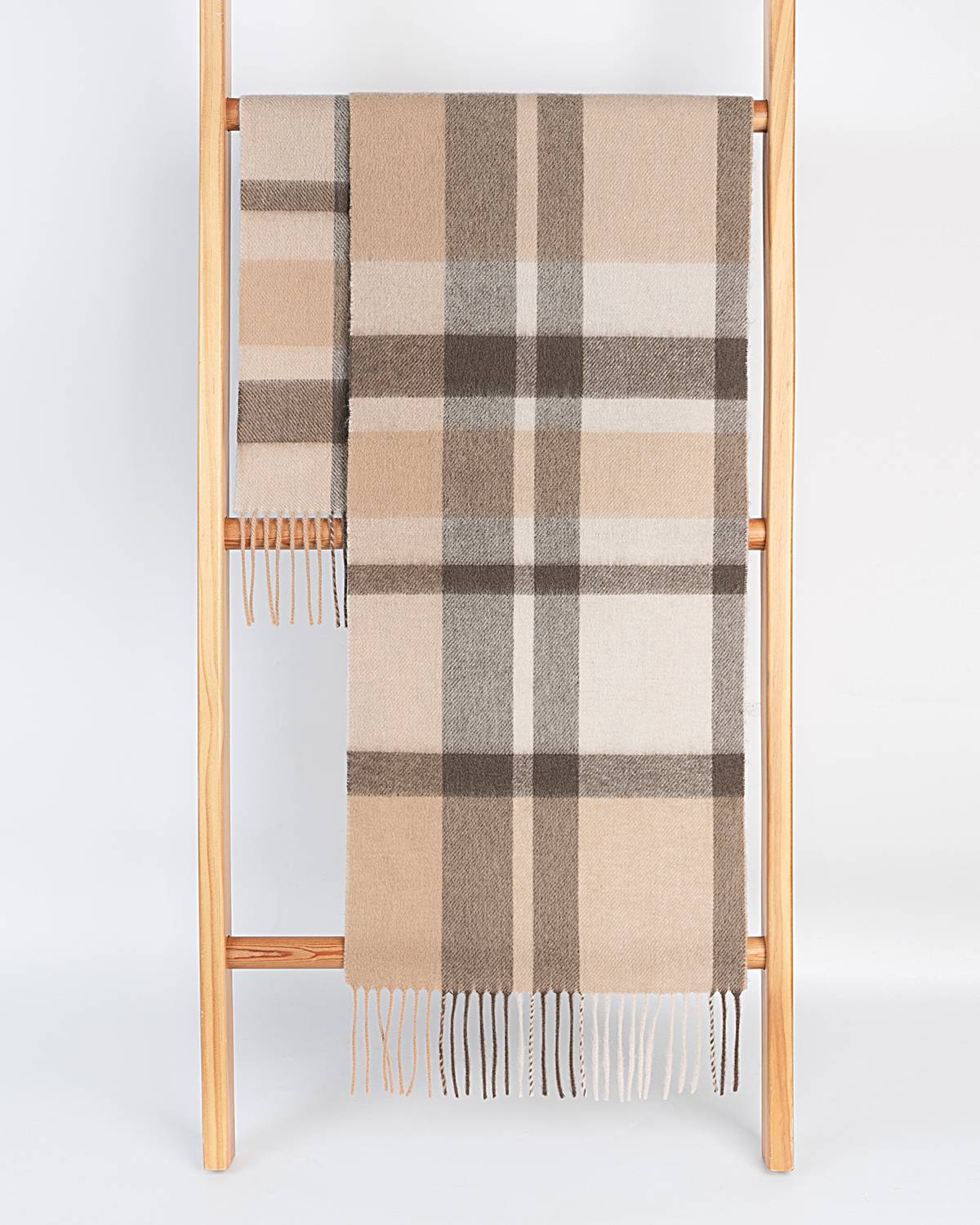 A gray and coffee plaid scarf draped over a wooden ladder, showcasing its stylish pattern.