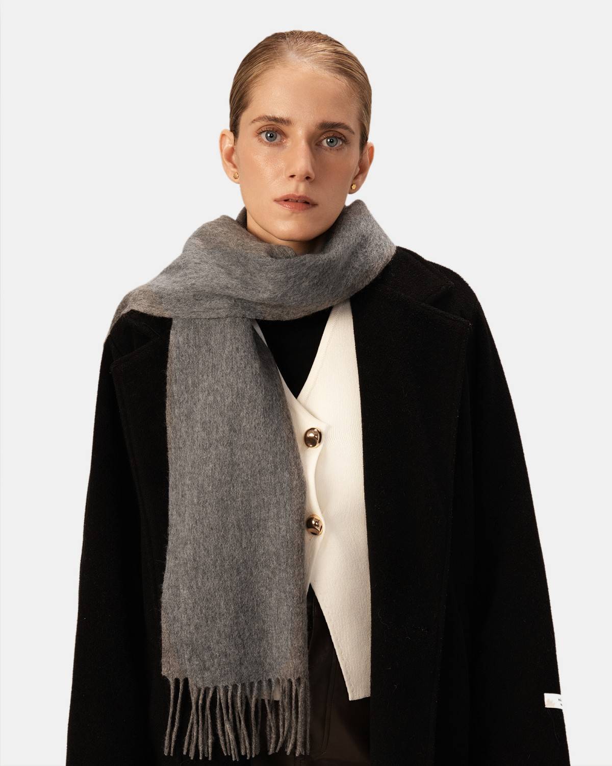A woman wearing a stylish black coat paired with a warm gray winter scarf, suitable for winter outings.