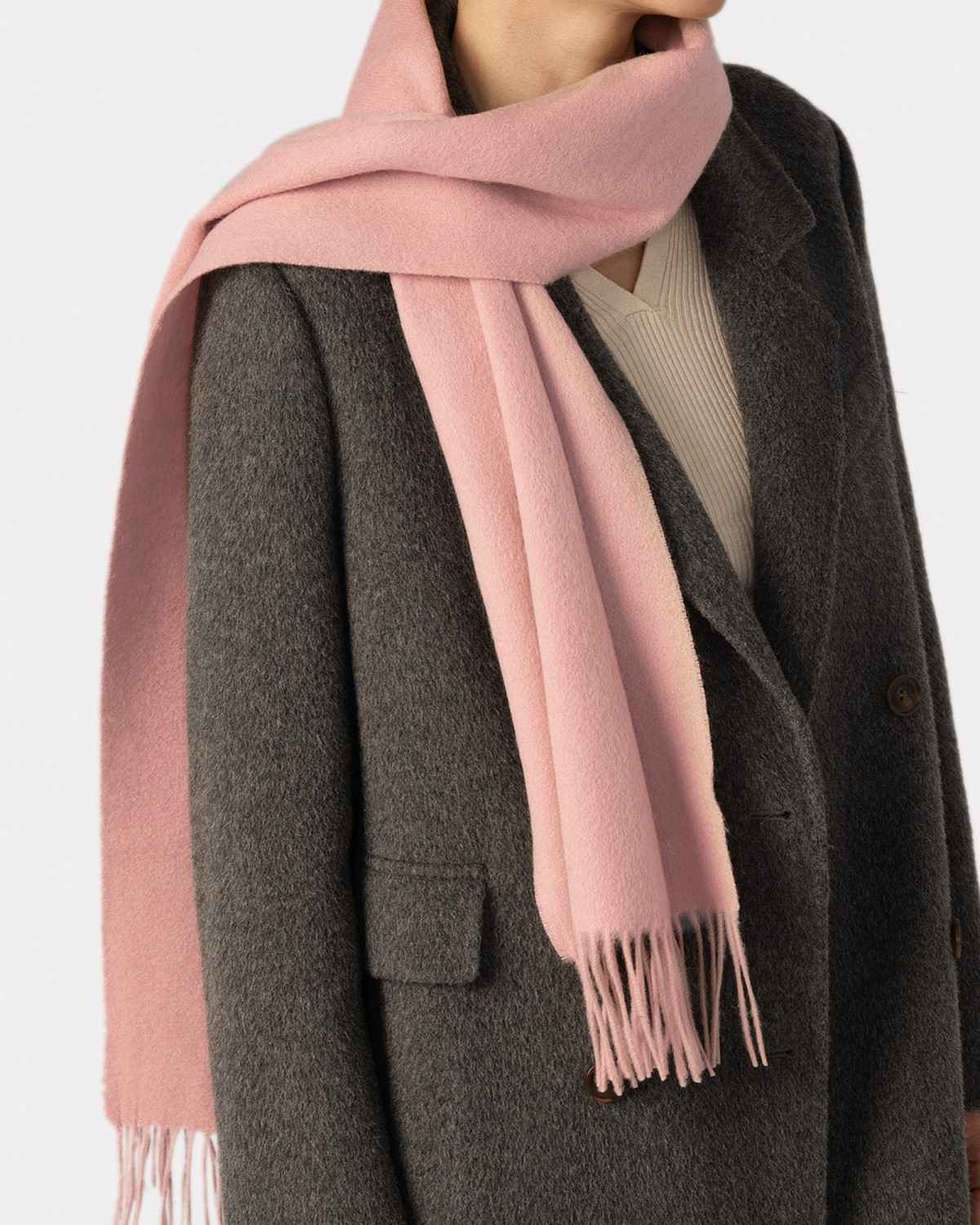 A woman in a grey coat elegantly wears a pink winter scarf, showcasing a stylish and cozy look.