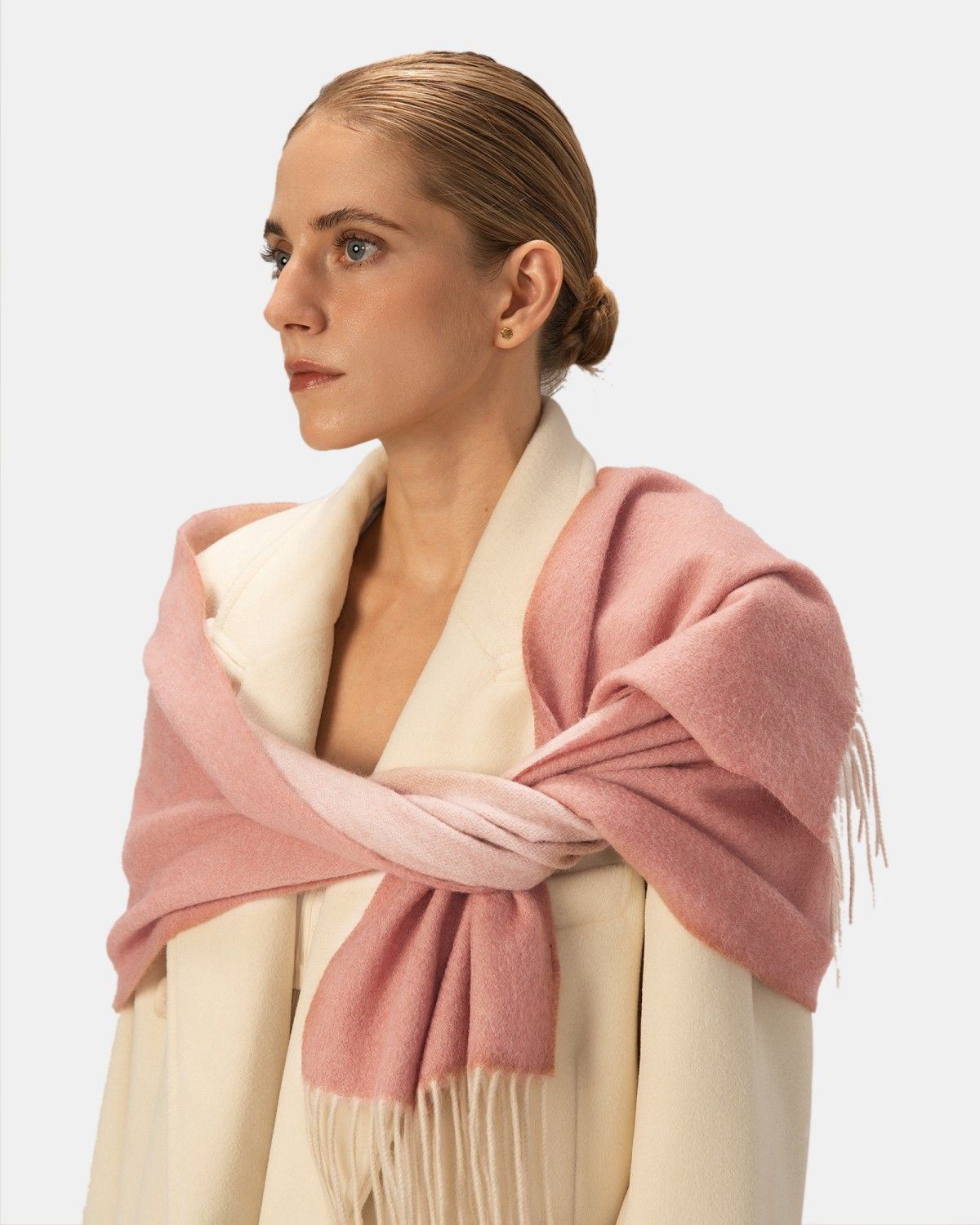 A woman elegantly wears a reversible scarf in pink and light pink, highlighting its chic and fashionable appeal.