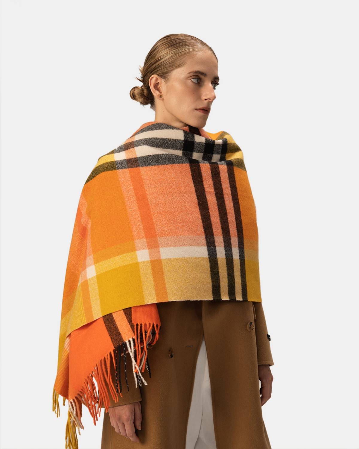 A woman stylishly draped in a vibrant orange, yellow, and black plaid shawl, showcasing her unique fashion sense.