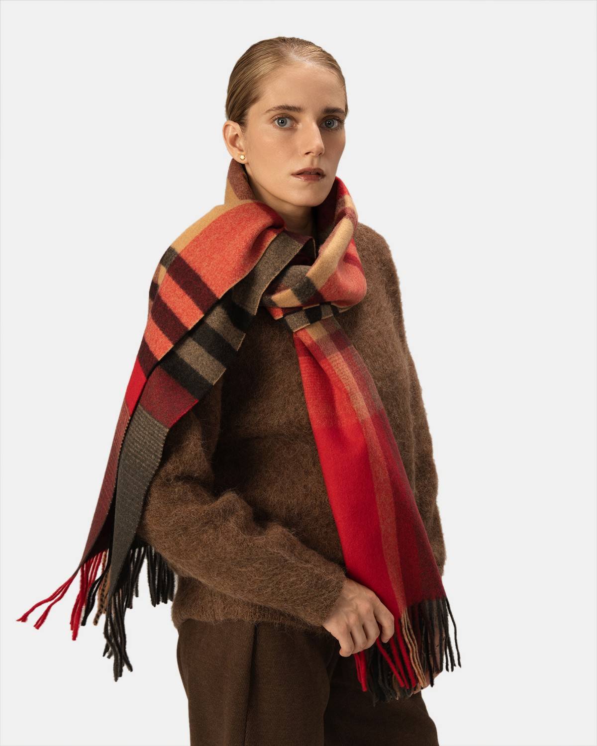 A woman elegantly draped in a vibrant red, black, and brown scarf, showcasing her stylish accessory.